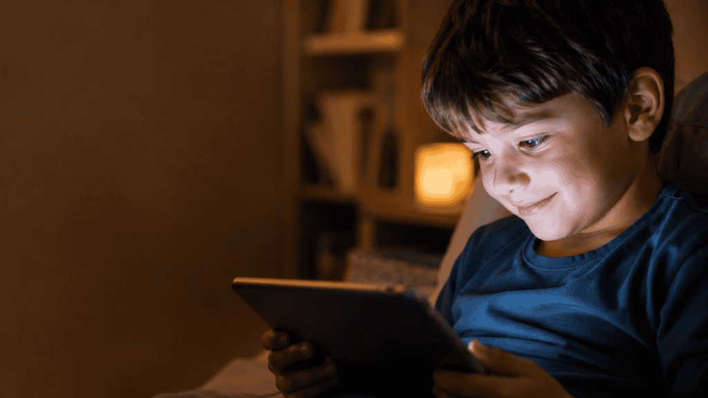 A child smiles at a tablet screen in a calm, softly lit room, showing screen time as part of a predictable daily routine.